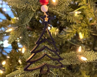 May include: A dark brown Christmas tree ornament hanging on a green Christmas tree. The ornament is shaped like a tree and has a star at the top. The ornament is suspended by a string with wooden beads. The tree is decorated with white lights.