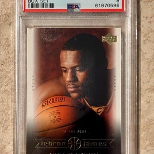 Könnte beinhalten: Eine 2003 Upper Deck LeBron James Box Set Sammelkarte, bewertet von PSA. Die Karte zeigt ein Porträt von LeBron James mit einem Basketball. Die Karte befindet sich in einer Schutzhülle.