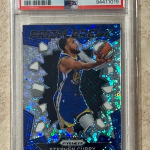 May include: A Stephen Curry basketball card from the 2023 Prizm set, featuring a blue and silver design. The card is graded GEM MT 10 by PSA and includes the text "PRIZM BREAK-FAST BREAK". The card is encased in a protective holder.