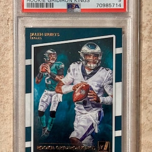May include: A graded 2020 Panini Donruss Jalen Hurts Rookie Gridiron Kings trading card. The card features a photo of Jalen Hurts in an Eagles uniform. The card is graded a 9 by PSA and is encased in a protective holder.