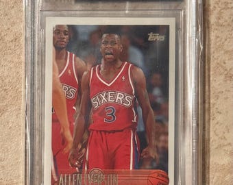 May include: A 1996-97 Topps Allen Iverson basketball card, graded 8.5, encased in a protective holder. The card features Iverson in a red Sixers jersey with the number 3. The card's text includes "ALLEN IVERSON" and "TOPPS".