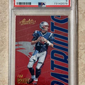 Puede incluir: Una tarjeta de fútbol de Tom Brady de 2018 Panini Absolute, calificada como Mint 9 por PSA, en un soporte protector. La tarjeta presenta a Brady con su uniforme de los New England Patriots, sobre un fondo rojo y blanco. Mide aprox. 6,35 cm x 8,89 cm.