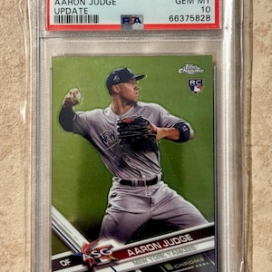 May include: A 2017 Topps Chrome baseball card featuring Aaron Judge of the New York Yankees. The card is graded GEM MT 10 and encased in a protective holder. The card has a green background and the player is in action.