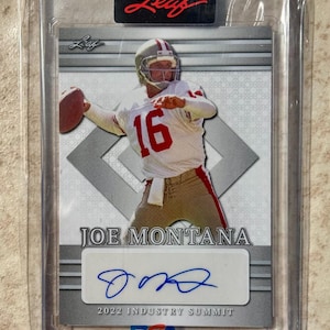 Könnte beinhalten: Eine Joe Montana Football-Sammelkarte in einer Schutzhülle. Die Karte zeigt Montana beim Werfen eines Footballs, mit einem weißen Trikot mit der Nummer 16. Die Karte enthält seine Unterschrift und den Text "2022 Industry Summit".