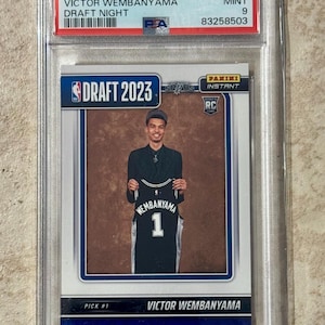 May include: A 2023 Panini Instant Victor Wembanyama Draft Night trading card graded PSA Mint 9. The card features a photograph of Victor Wembanyama holding a black San Antonio Spurs jersey with the number 1. Text includes DRAFT 2023 and PICK #1.