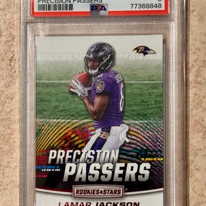Puede incluir: Una tarjeta comercial calificada con Lamar Jackson con un uniforme púrpura de los Baltimore Ravens, sosteniendo un balón de fútbol. La tarjeta es de la serie 2018 Panini Precision Passers, calificada como Mint 9 por PSA.