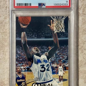 May include: A 1994 Stadium Club Shaquille O'Neal basketball trading card, graded Mint 9 by PSA. The card features O'Neal in a white and blue pinstripe jersey, reaching for a basketball near a hoop, with the text Shaquille O'Neal and number 32.
