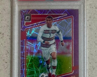 May include: A 2021/22 Donruss Road to Qatar Cristiano Ronaldo Optic-Purple Velocity trading card, graded PSA Gem Mt 10. The card features a purple holographic pattern, a photo of Ronaldo in a white Portugal kit, and the text Cristiano Ronaldo.