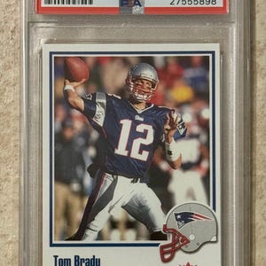May include: A 2002 Fleer Throwbacks Tom Brady trading card, graded as Mint 9 by PSA. The card features Tom Brady in a New England Patriots uniform throwing a football. The card is encased in a protective holder.