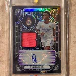 May include: A collectible sports card featuring Vinícius Jr. of Real Madrid. The card has a red patch and an autograph. The card is encased in a protective holder with the PSA logo.