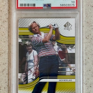 Op de afbeelding: Een 2012 SP Authentic Golf trading card met Jack Nicklaus in een rood, wit en blauw gestreept shirt. De kaart is beoordeeld als GEM MT 10 en zit in een beschermende houder. De tekst "2012 SP AUTHENTIC GOLF JACK NICKLAUS" is zichtbaar.