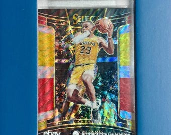 Peut inclure: Une carte de basket-ball 2019 Panini Select LeBron James Tri-Color Prizm notée PSA Gem Mt 10. La carte présente un fond holographique jaune et doré avec un joueur portant un maillot jaune des Los Angeles Lakers tenant un ballon de basket.