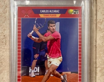 May include: A 2023 Leaf Web Exclusives Carlos Alcaraz trading card graded Mint 9 by PSA. The card features a photograph of the tennis player in a pink shirt and white shorts on a clay court, with the text Carlos Alcaraz, Tennis Player, and Pro Set.