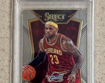 May include: A 2014 Panini Select LeBron James basketball trading card, graded GEM MT 10 by PSA. The card features LeBron James in a red Cleveland Cavaliers jersey with the number 23, holding a basketball, encased in a clear protective plastic slab.
