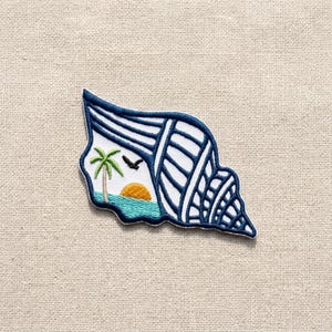 May include: An embroidered patch shaped like a seashell with a dark blue border. The design features a white background with dark blue stripes, a green palm tree, a yellow sun, a turquoise sea, and a small black bird silhouette in the center.