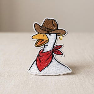 May include: Embroidered patch featuring a cartoon goose wearing a brown cowboy hat, a red bandana, and a gold hoop earring. The goose has a white body, a yellow beak, and is outlined in white.