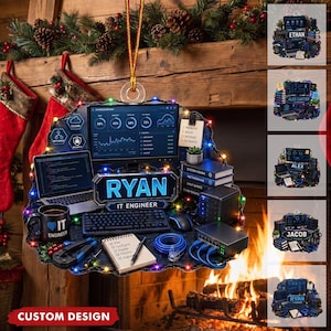 May include: A decorative ornament featuring a computer workstation with a monitor displaying data, a laptop, a keyboard, a mouse, a mug labeled IT ENGINEER, a notebook, and networking equipment, all illuminated by colorful string lights.