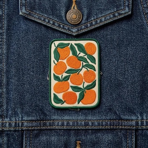 May include: Embroidered patch featuring a vibrant orange and green design of oranges and leaves. The patch has a white background with a green border. The patch is attached to a blue denim jacket.