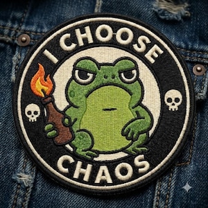 May include: A circular embroidered patch featuring a green frog holding a brown bottle with a lit orange and yellow flame. The design includes two small white skulls on the sides and the text I CHOOSE CHAOS in white lettering on a black border.