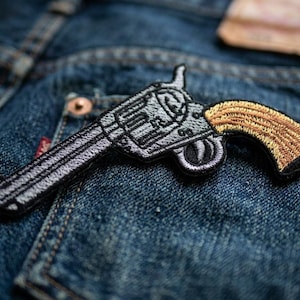 May include: A white ceramic mug with a black handle and the text "But First, Coffee" in a black, handwritten-style font. The mug is on a white surface.