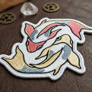 May include: Embroidered patch featuring two koi fish in a yin-yang design. The patch has a white background with the fish detailed in pink, yellow, and blue. The patch is surrounded by a white border.