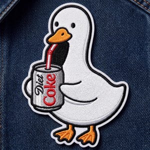 May include: An embroidered patch featuring a white duck with an orange beak and feet, holding a silver soda can with a red straw. The can has the text Diet Coke printed in black and red. The patch is attached to a dark blue denim fabric background.