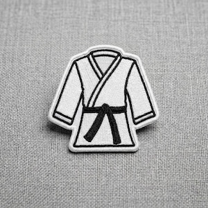 May include: A white karate gi patch with a black belt, outlined in black. The patch is a stylized representation of a martial arts uniform, perfect for adding to clothing or accessories.