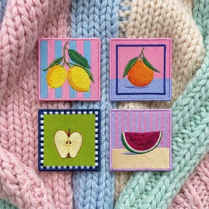 May include: Four square embroidered patches featuring fruit designs. One shows two yellow lemons on a pink and blue striped background, another an orange on a pink and blue field, a third a halved apple on green, and the last a watermelon slice.