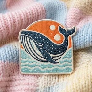 May include: A semi-circular embroidered patch featuring a dark blue whale with white spots swimming in light blue waves. The background shows a vibrant orange sun with two white circular accents. The patch has a clean white border edge.