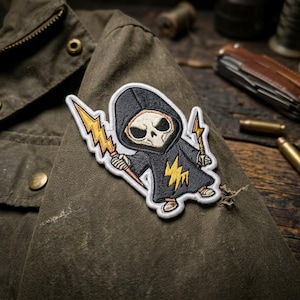 May include: Embroidered patch featuring a cartoon Grim Reaper character in a black hooded cloak, holding yellow lightning bolts. The patch is sewn onto a dark green jacket, with a zipper and brass buttons visible.