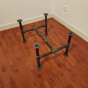 Pode incluir: Base de mesa de estilo industrial feita de tubos e acessórios de metal cinza escuro. A base tem quatro pernas com placas de montagem circulares e uma estrutura retangular. Os tubos são conectados com acessórios roscados, criando um design resistente e funcional.