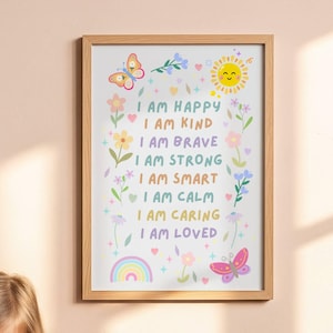 May include: A framed wall art print featuring a light-colored wooden frame and a white background with colorful illustrations of a sun, butterflies, flowers, and a rainbow. The text reads: I AM HAPPY, I AM KIND, I AM BRAVE, I AM STRONG, I AM SMART, I AM CALM, I AM CARING, I AM LOVED.