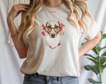 Puede incluir: Camiseta color crema con un perro salchicha con gafas. Las orejas y el pecho del perro tienen un patrón de cuadros rojos y blancos. La cara del perro está detallada con pelaje marrón y barba blanca. La camiseta es de estilo casual.