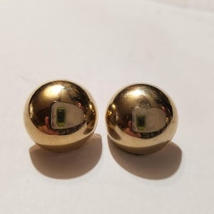 May include: A pair of polished gold-tone spherical stud earrings with a smooth, reflective surface. Each earring features a rounded, dome-like shape that catches light, creating a bright, metallic appearance suitable for various jewelry collections.