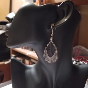 May include: A teardrop-shaped dangle earring featuring a silver-toned metal frame wrapped with thin, dark gray thread in a geometric string art pattern. The earring hangs from a simple silver-toned hook wire, creating a delicate, openwork design.