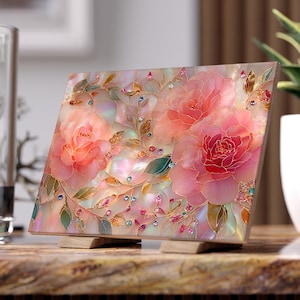 May include: Square decorative art piece with a floral design. It features pink roses, green leaves, and sparkling accents. The artwork is displayed on a wooden stand, showcasing a blend of colours and textures.