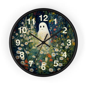 May include: A round wall clock with a black frame featuring a central illustration of a small white ghost standing in a dense field of white daisies and colorful wildflowers. The clock face displays large, cream-colored numerals from 1 to 12.