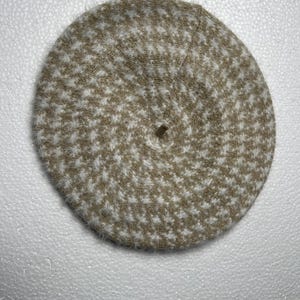 May include: A beige and white houndstooth pattern beret. The hat is round with a small hole at the center. The beret is made of a soft, textured material. This classic accessory is suitable for various occasions.