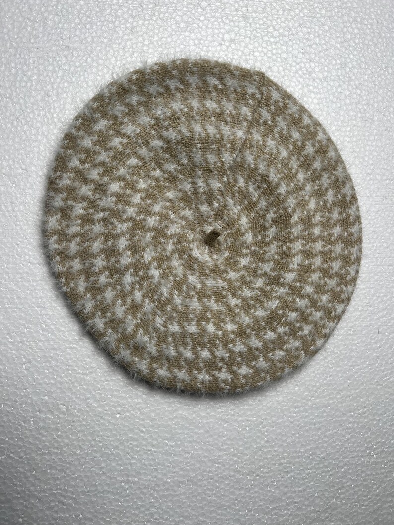 May include: A beige and white houndstooth pattern beret. The hat is round with a small hole at the center. The beret is made of a soft, textured material. This classic accessory is suitable for various occasions.