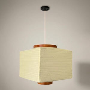 May include: A square pendant light fitting featuring a cream-coloured paper shade with horizontal ribbed texture. The shade is held by a dark brown wooden frame at the top and bottom, suspended from the ceiling by a thin cord and a black circular canopy.