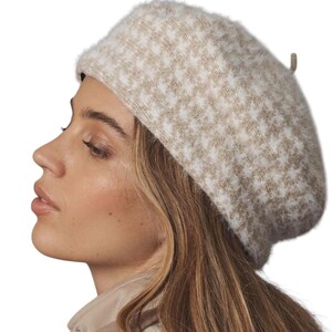 May include: A beige and white houndstooth pattern beret. The hat is made of a soft, fuzzy material. The beret is a classic style, perfect for adding a touch of elegance to any outfit. The hat is a neutral color, making it versatile for various ensembles.