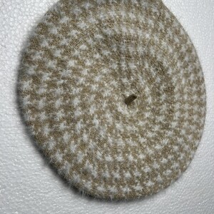 May include: A round, beige and white patterned beret. The hat features a houndstooth design and is made of a soft, textured material. The beret is a classic accessory, suitable for various outfits and occasions.