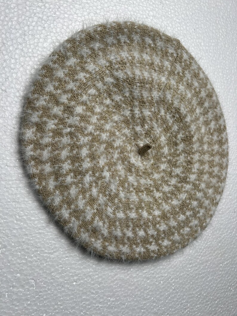 May include: A round, beige and white patterned beret. The hat features a houndstooth design and is made of a soft, textured material. The beret is a classic accessory, suitable for various outfits and occasions.