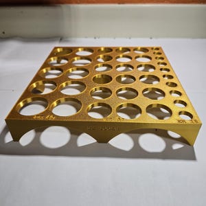 May include: A gold-colored tool organizer with multiple circular openings of varying sizes. The organizer has a rectangular shape with a curved base and the text "SZ TOOLS" is visible. The tool organizer is designed to hold various tools.
