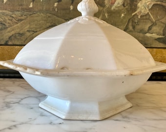 May include: White porcelain serving dish with a lid. The dish is octagonal and has a raised rim. The lid has a knob in the center.