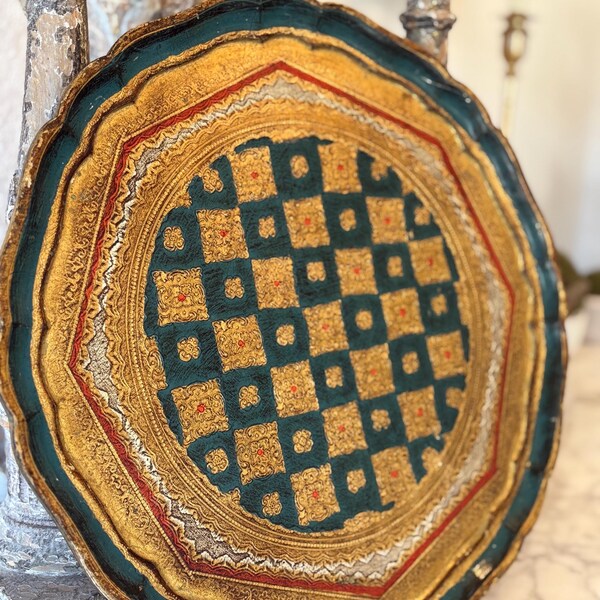 Puede incluir: Una bandeja redonda pintada en oro con un borde azul verdoso y diseños intrincados en oro y rojo. El centro de la bandeja presenta un patrón de cuadros en azul verdoso y oro.