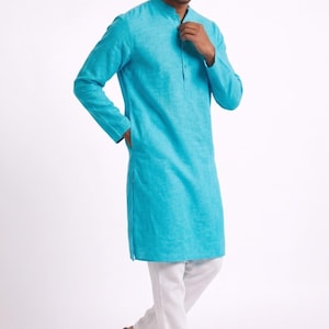 May include: A turquoise long-sleeved tunic with a mandarin collar and a buttoned placket. The tunic is paired with white pants and brown sandals. The outfit is suitable for casual or semi-formal wear.