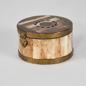 May include: A round, antique box with a hinged lid. The lid is made of wood and inlaid with light and dark wood in a geometric pattern. The sides of the box are made of vertical ivory-colored pieces. The box is trimmed with brass and has a brass clasp.