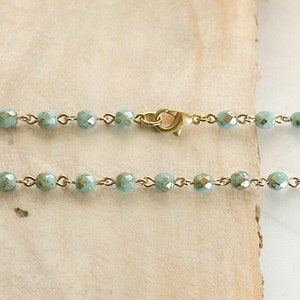 May include: A delicate gold chain necklace with light blue faceted beads. The necklace has a lobster clasp closure.