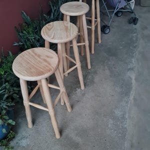 Pode incluir: Quatro bancos de bar de madeira com assentos redondos e quatro pernas. Os bancos são feitos de madeira clara e estão dispostos em fila. Adequados para uma cozinha ou bar.